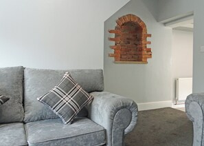 A grey sofa with a plaid pillow, a brick wall arch, and a radiator in the background. - A beautifully restored two-storey, two bedroom cottage sleeping four people. (Filey)