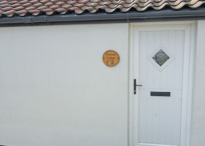 A white door with a small round sign above it and a diamond-shaped window above the door. - A beautifully restored two-storey, two bedroom cottage sleeping four people. (Filey)