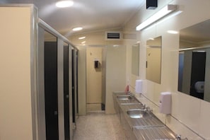 Un bany d'hotel amb diverses dutxes, un assecagats mans i un mirall.