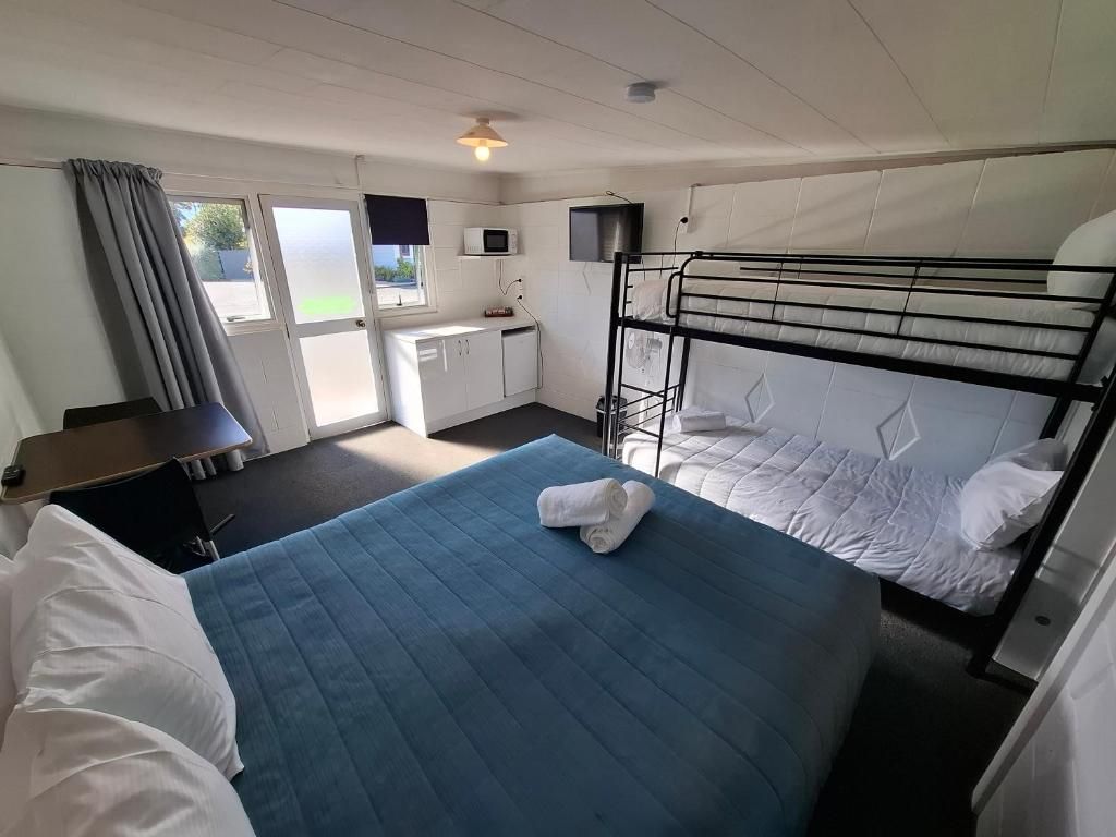 Une chambre d’hôtel avec un lit superposé, un bureau avec une chaise, un four à micro-ondes et une fenêtre avec des rideaux.