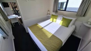 Habitación de hotel con cama, mesita de noche, lámpara, ventana con cortinas y vistas al exterior.