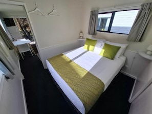 Habitació d'hotel amb llit, una taula de nit, una làmpada, una finestra amb cortines i vista a l'exterior.