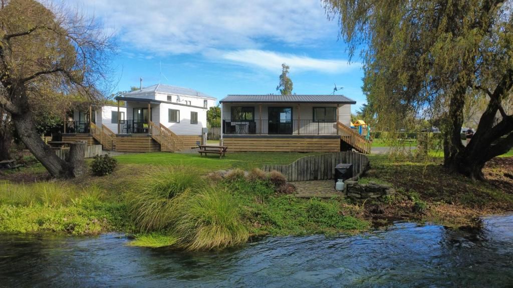 Une propriété située au bord de la rivière, dotée d’une terrasse en bois, d’un petit pont et d’une zone herbeuse.