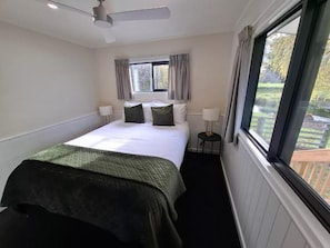 Habitación de hotel con cama, ventana, ventilador de techo y vista al exterior.