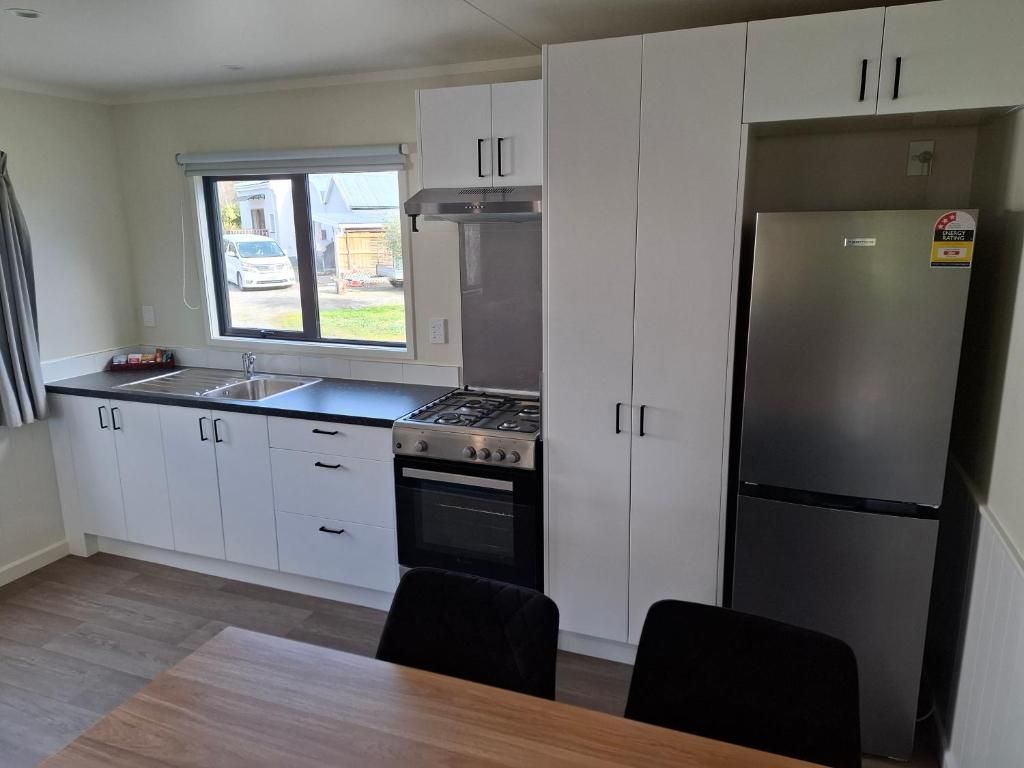 Una cocina moderna con armarios blancos, un refrigerador de acero inoxidable, una estufa y una ventana con vistas al exterior.