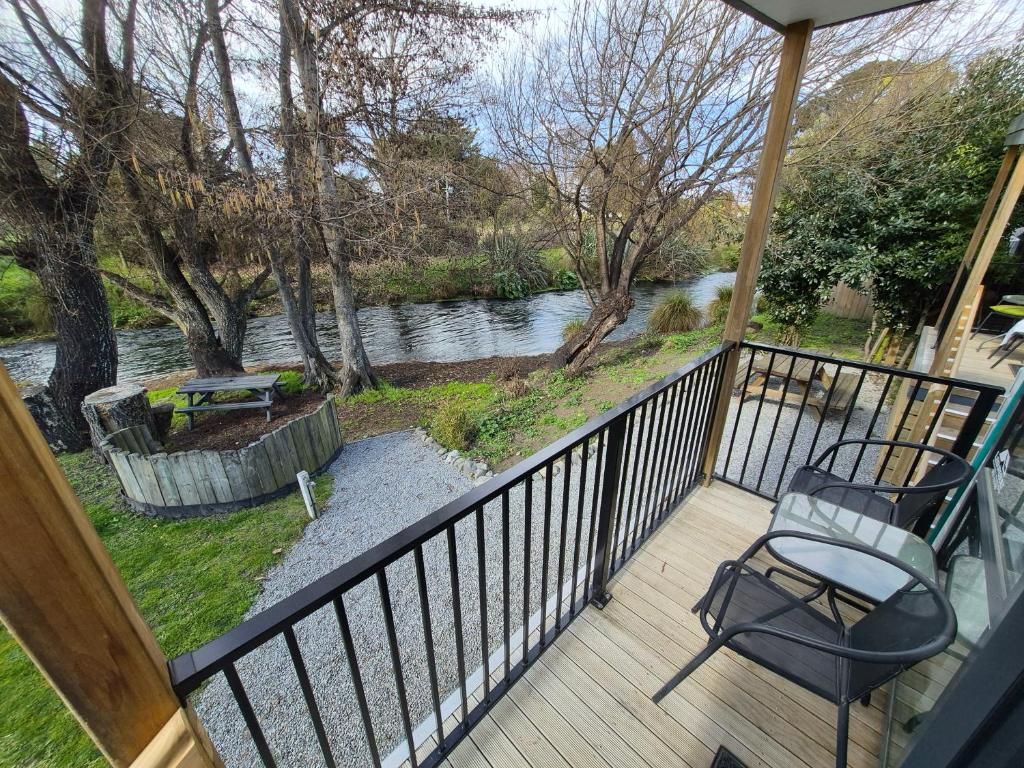 Une terrasse avec vue sur une rivière et des arbres, une table de pique-nique et une table en verre avec des chaises.