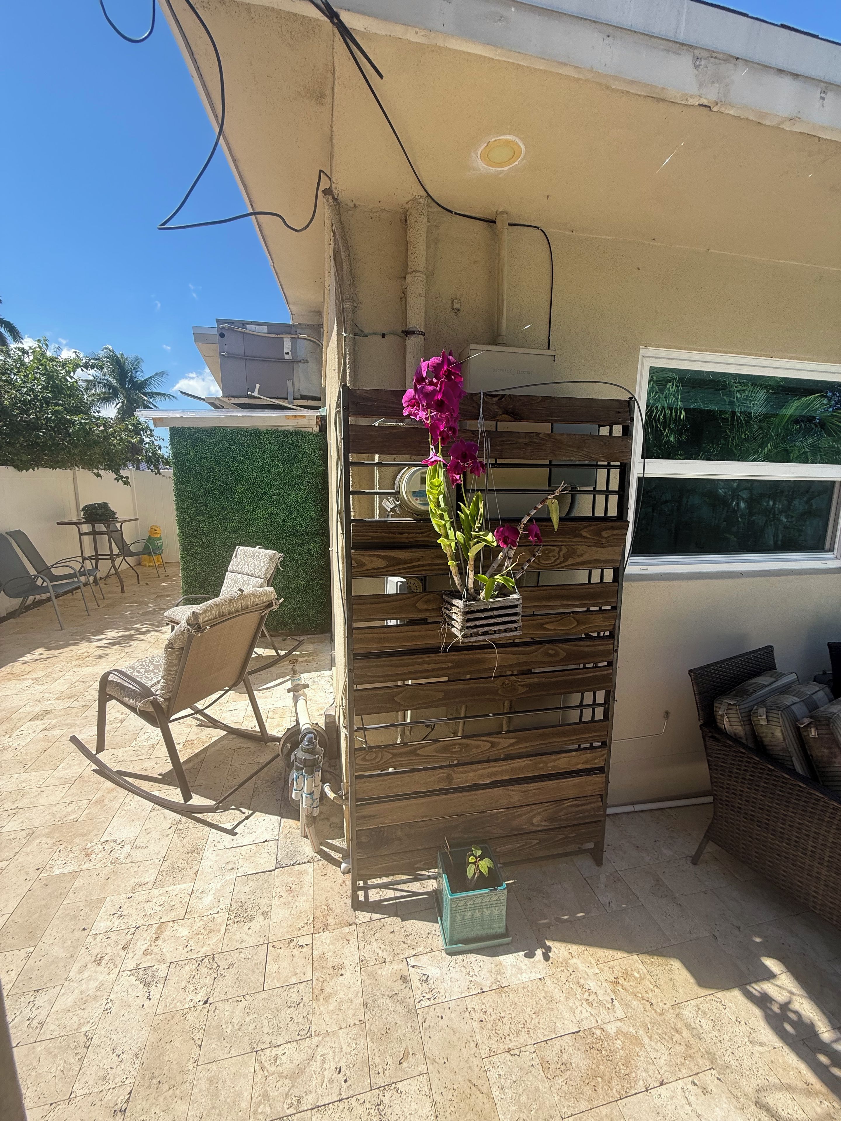 Un espacio al aire libre con una jardinera de madera con flores, una mecedora y un sofá de mimbre.
