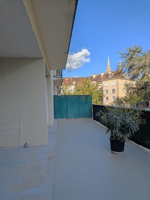 Ein Balkon mit einem Topfpflanzen, einem grünen Zaun und Gebäuden im Hintergrund.