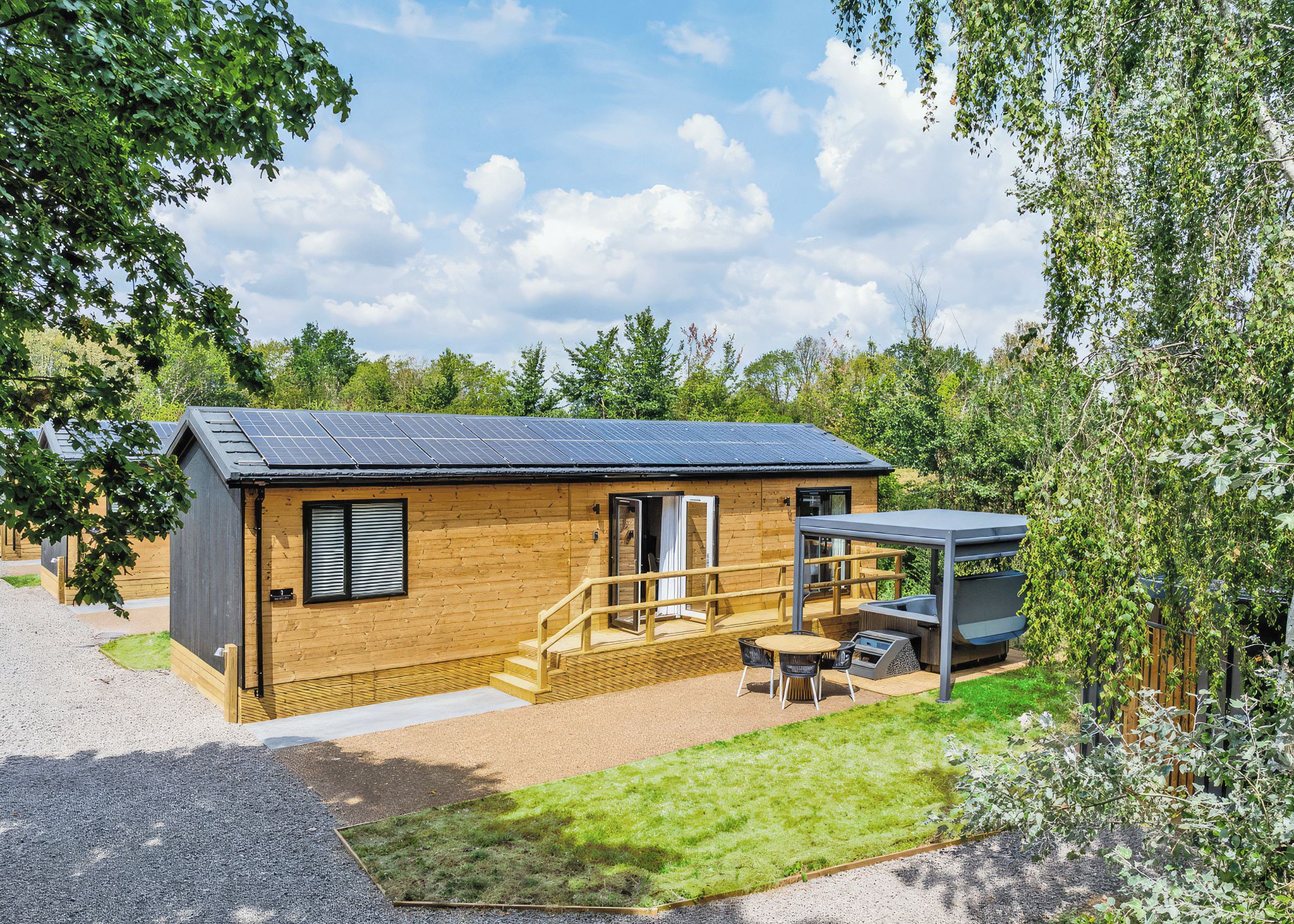 A wooden cabin with a solar panel roof, a patio with outdoor seating, and a covered area with a grill.