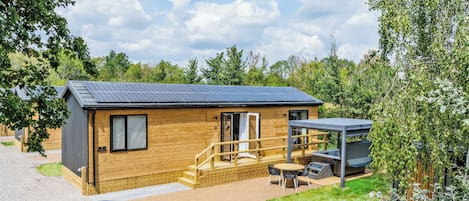 A wooden cabin with a solar panel roof, a patio with outdoor seating, and a covered area with a grill.
