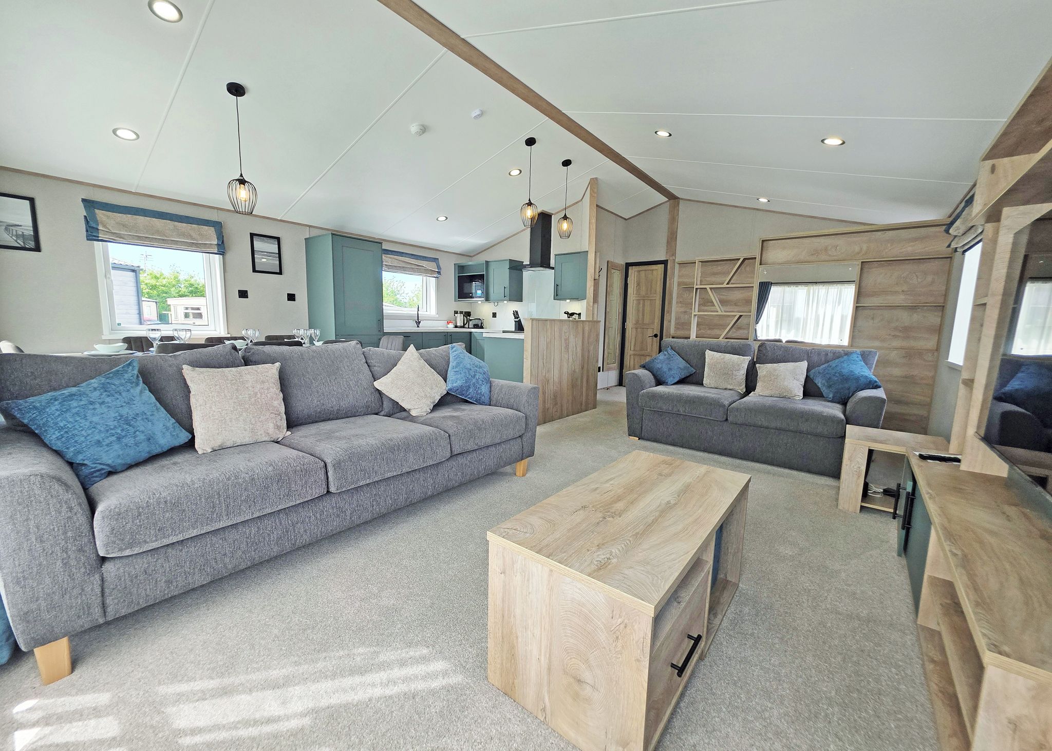 Een moderne woonkamer met een grijze bank, een houten salontafel en een keuken op de achtergrond.