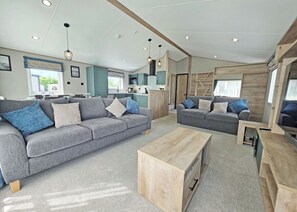 A modern living room with a grey sofa, a wooden coffee table, and a kitchen area in the background. - Platinum 8 Berth Lodge (Mablethorpe)