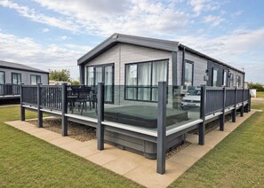 A modern mobile home with a glass balcony, outdoor seating, and a clear sky. - Platinum 8 Berth Lodge (Mablethorpe)