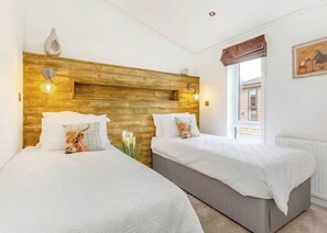 Ein Hotelzimmer mit zwei Betten, einem Holzkopfteil, Wandleuchten, einem Fenster mit Blick und einer Heizung.