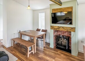 Ein Zimmer mit einem Holztisch, Stühlen, einer Bank, einem Kamin und einem darüber hängenden Fernseher.