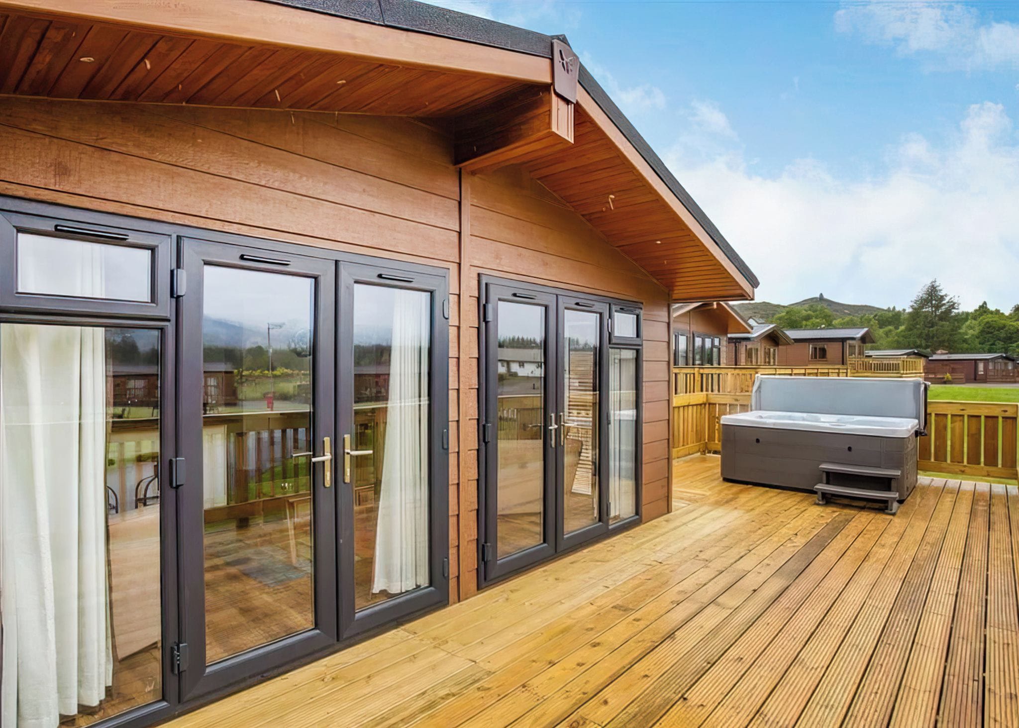 A wooden deck with a barbecue grill, large sliding glass doors, and a view of a residential area.