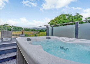 Ein Whirlpool mit Blick auf eine Landschaft, eine Holzterrasse und ein Metallzaun.