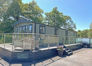 Een moderne camper met een overdekt terras, buitenzitplaatsen en een bordje met 'HV3 Bassenthwaite'.