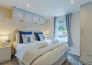 A hotel room with a bed, a nightstand, a wardrobe, and a window with curtains. - Premium 2 bed holiday home with hot tub Pet (Bassenthwaite, near Keswick)