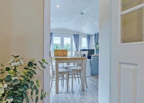A hallway leading to a dining area with a table and chairs, a window with curtains, and a plant. - Premium 2 bed holiday home with hot tub Pet (Bassenthwaite, near Keswick)