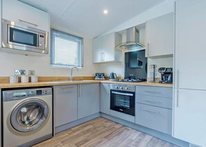 Een kleine keuken met een wasmachine, magnetron, oven en een koffieapparaat.