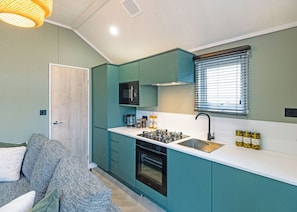 A compact kitchen with teal cabinetry, a built-in microwave, a gas stove, and a window with blinds. - A stylish one-bedroom retreat designed exclusively for couples. (Workington)