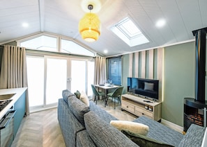 A modern living room with a sofa, TV, fireplace, dining area, and large windows. - A stylish one-bedroom retreat designed exclusively for couples. (Workington)