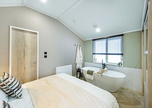 Ein Schlafzimmer mit einem großen Bett, einer eingebauten Badewanne und einem Fenster mit Jalousien.