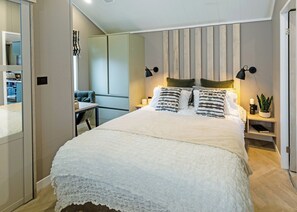 Ein modernes Schlafzimmer mit einem großen Bett, Nachttischen, einem Schreibtisch und Blick auf die Küche.