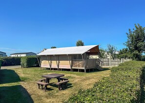 A camping area with a tent, picnic table, and surrounding greenery. - Sea View Safari Tents (Hemsby)