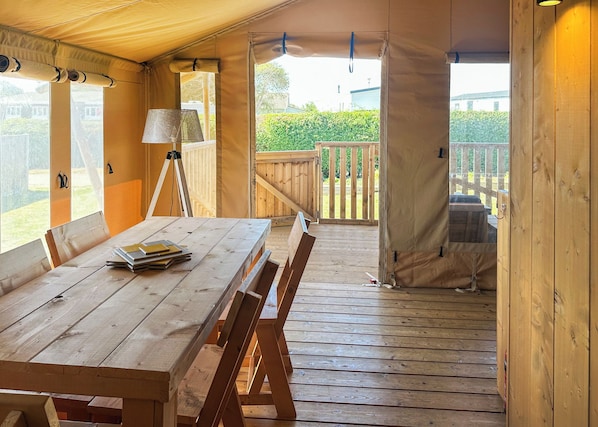 A wooden deck with a table and chairs, a lamp, and a view of a garden.