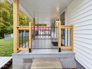 Een overdekte veranda met houten spijlen, een betonnen trap en een metalen poort.