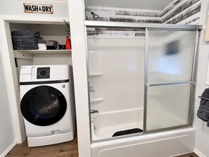 A compact laundry room with a washing machine, a drying rack, and a shower enclosure. - Lick Creek Pit Stop   
Dog friendly  
Direct trail access 
2 Kings 2 Queens (Williamson)