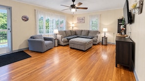 Una sala de estar con sofá, sillón, reposapiés y televisor sobre un mueble.