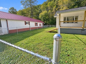 A fenced yard with a metal gate, a grassy area, and a building with a red roof. - Lick Creek Pit Stop   
Dog friendly  
Direct trail access 
2 Kings 2 Queens (Williamson)