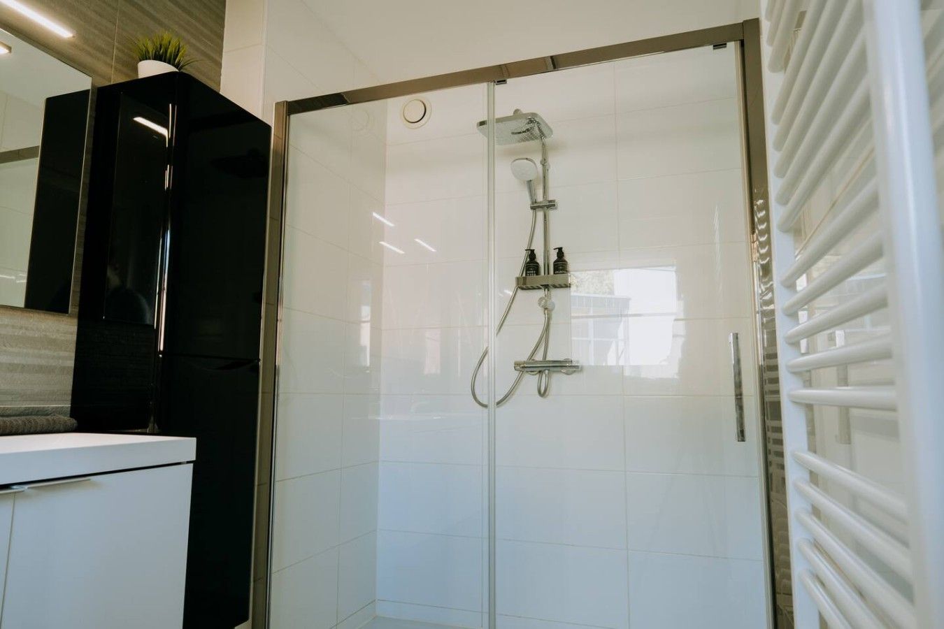 Une salle de bain moderne avec une douche à parois de verre, des murs recouverts de carreaux blancs et un meuble intégré.