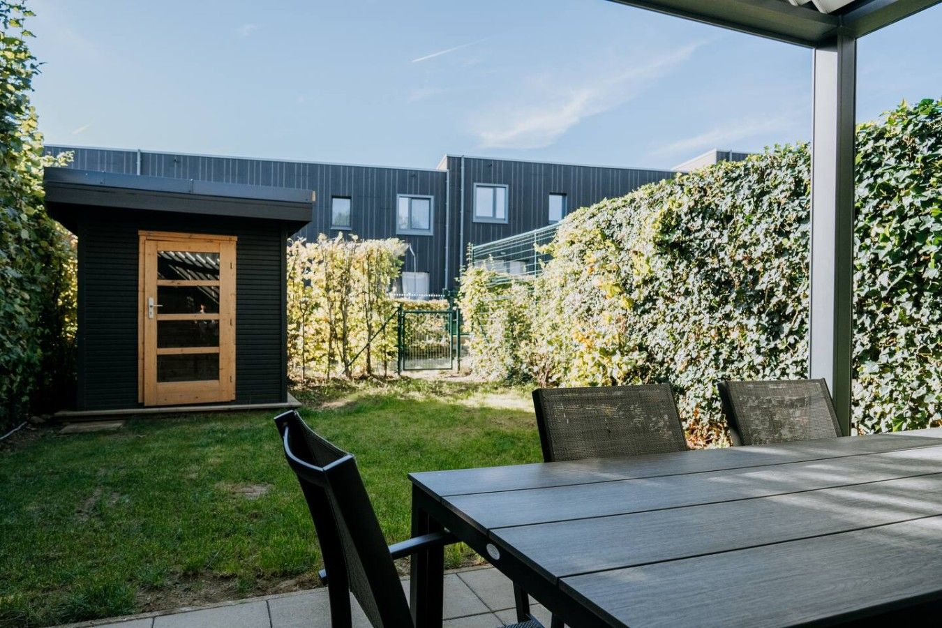 Une terrasse avec une table et des chaises, une porte en bois et, au fond, un bâtiment moderne.