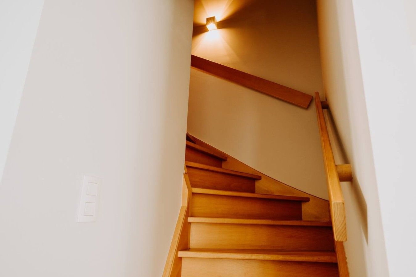 Un escalier en bois, doté d’une rampe et d’un luminaire fixé au mur.