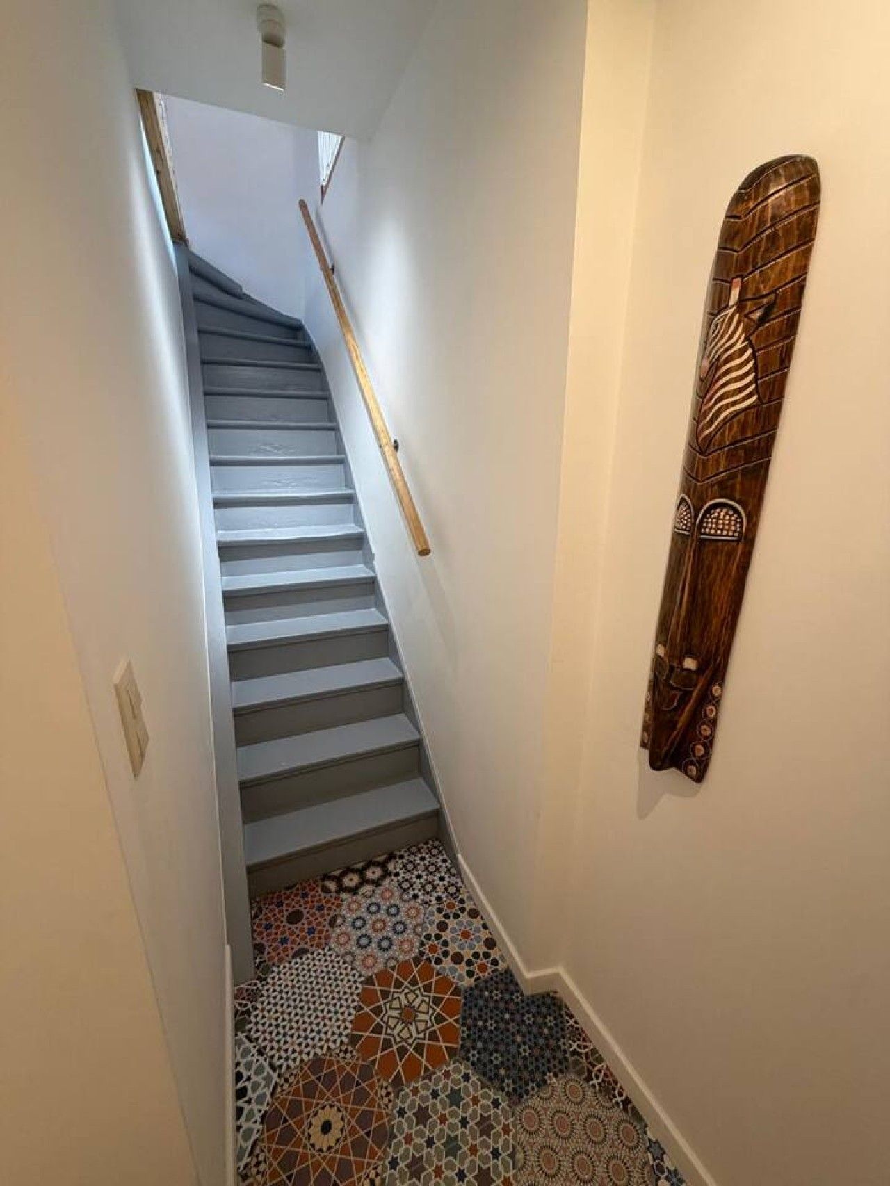 Een trap met een houten leuning en vloertegels met een patroon.
