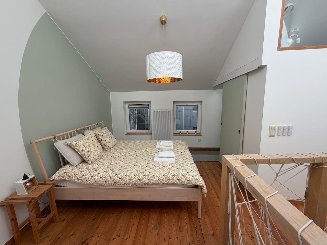 Une chambre à coucher avec un lit, un luminaire suspendu, une fenêtre et un banc en bois.