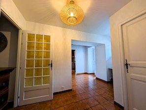 A hallway with a tiled floor, a door with a frosted glass panel, and a hanging light fixture.