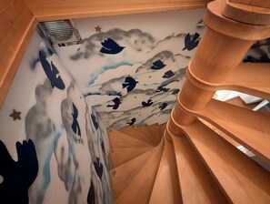 A wooden spiral staircase with a wall mural depicting birds and clouds.