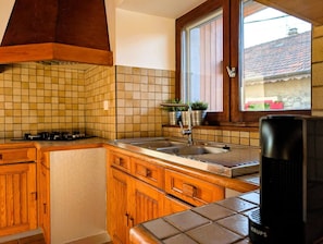A kitchen with wooden cabinets, a tiled backsplash, a window with a view, and a stove. - Authentic Lake Geneva farmhouse near Évian (Larringes)