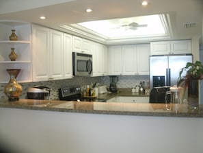 A kitchen with white cabinets, a microwave, a refrigerator, and a ceiling fan. - Direct Beach Front -- Sun, Sand, Luxury and Fun (Bonita Springs)