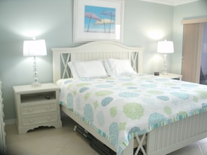 A bedroom with a bed, two bedside tables, a nightstand, a lamp, and a framed picture on the wall. - Direct Beach Front -- Sun, Sand, Luxury and Fun (Bonita Springs)