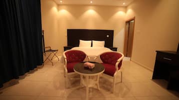 Ein Hotelzimmer mit einem Bett, zwei roten Polsterstühlen, einem kleinen runden Tisch und einem schwarzen Nachttisch.