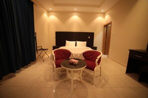 Habitación de hotel con cama, dos sillones tapizados en rojo, una mesita redonda y una mesita de noche negra.