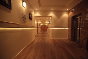 Ein Hotelgang mit Holzböden, Wandleuchten und einem Empfangsbereich mit Theke.