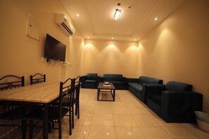 A living room with a dining table, chairs, sofas, and a flat-screen TV mounted on the wall. - Rawnaq Almansak (Abha)