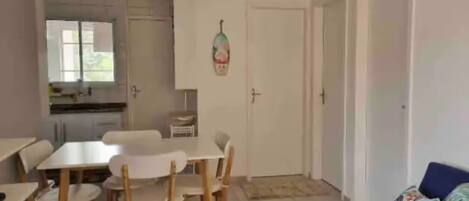 A room with a dining table and chairs, a sofa, a kitchen area with cabinets, and an air conditioning unit.